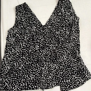 Svartvit prickig linnetopp - Snygg svart linnetopp med vita prickar och djup v-ringning. Toppen är ärmlös och har en lätt utsvängd passform som ger en avslappnad vibe. Perfekt att matcha med jeans eller kjol för en cool look.