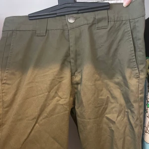 Olivgröna chinos från saligia lager 157 - Snygga olivgröna chinos från Saligia med klassisk passform. Byxorna har bälteshällor, knappstängning och två bakfickor, varav en med knapp. Perfekta för en clean och stilren look.