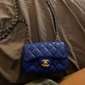 Blå quiltad axelväska i skinn - Supersnygg blå axelväska i quiltat skinn med klassisk guldfärgad kedja. Väskan har en kompakt form och ikonisk design, perfekt för att lyfta vilken outfit som helst. Insidan är fodrad i rött. Kan tänka mig sänka vid en snabb affär 