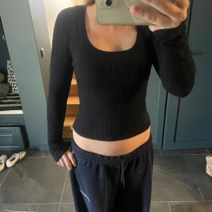 Svart ribbad långärmad tröja Gina Tricot - Svart långärmad tröja från Gina Tricot med ribbad struktur och rundad, djup urringning. Sitter tight och har en smickrande passform som framhäver figuren. Perfekt att styla med jeans eller kjol för en clean look.