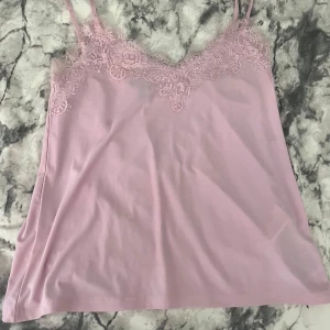 Ljusrosa linnetopp med spets från Amisu - Supersöt ljusrosa linnetopp från Amisu med tunna axelband och vacker spetsdetalj längs urringningen. Toppen har en mjuk, flowy känsla och är perfekt för att ge outfiten en romantisk touch. Passar dig som gillar feminina och stilrena plagg.