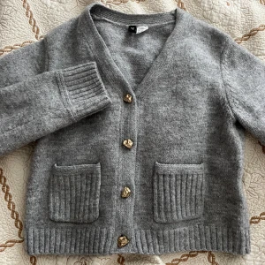 Grå kofta med guldknappar - Mysig grå kofta från H&M med snygga guldiga knappar och två ribbade fickor framtill. Koftan är stickad, har lång ärm och v-ringning. Perfekt för lager-på-lager och chill vibes.