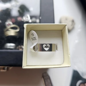 Silverring med hjärtformad detalj - Snygg och stilren silverfärgad ring i storlek 19 med ett urfräst hjärta framtill. Ringen har en bred, slät design som ger en modern vibe och passar perfekt för dig som gillar minimalistiska smycken med en twist.