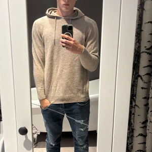 Beige stickad hoodie kashmir - Ny pris 800 kr. Snygg beige stickad hoodie med huva och snörning framtill. Tröjan har långärmade ärmar och ribbade muddar vid ärmslut och nederkant. Perfekt för dig som gillar chill och enkel stil, funkar till jeans eller joggers.  Använd ungefär 5 gånger, är skitskön och har bra passform jag växte ur den.