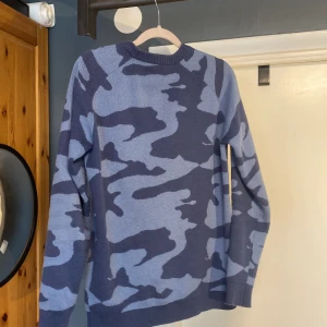 Camo stickad tröja - Snygg stickad tröja från C i blått camouflagemönster. Tröjan har rund halsringning, ribbade muddar och lång ärm. Perfekt för dig som gillar streetstyle och vill sticka ut lite extra med coolt mönster. Säljer pga att den är för liten för mig