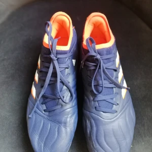 Adidas Copa blå fotbollsskor stl 41⅓ - Säljer ett par Adidas Copa fotbollsskor i mörkblått med vita och orange detaljer samt blå sula. Skorna har snörning och är fodrade med orange insida. Tillverkade i syntet och skinn för bästa känsla på planen.