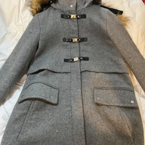Grå kappa med fuskpäls och spännen med huva  - Oanvänd med prislapp kvar men tappade bort en knapp på huva ( bild)