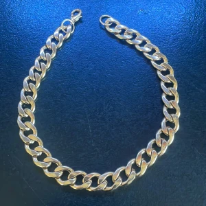 Kraftigt gukdigt halskedja - Säljer ett chunky halskedja i guld med breda, platta länkar och karbinlås. Perfekt statement piece för dig som gillar att sticka ut med accessoarer. Kedjan har en klassisk design som passar till många olika stilar.