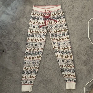 Mjukisbyxor med hundmönster från PJ Salvage - Supermysiga mjukisbyxor från PJ Salvage i vitt med gulligt mönster av franska bulldoggar, hjärtan och snöflingor i rött, blått och brunt. Byxorna har röd snörning i midjan, knappar framtill och muddar vid bensluten. Perfekta för chill dagar hemma!