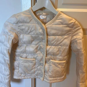 Beige quiltad pufferjacka Gina Tricot - Du kan prova att fråga för en pris sänkning!💕Quiltad beige pufferjacka från Gina Tricot med snygga flätade detaljer vid kanter och fickor. Jackan har tryckknappar framtill, två stora fickor och rund halsringning. Perfekt för dig som vill ha en stilren och trendig look.