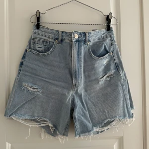 Ljusa jeansshorts från Stradivarius - Snygga ljusblå jeansshorts från Stradivarius med hög midja och råa, fransiga kanter. Shortsen har slitna detaljer både fram och bak för en cool, avslappnad vibe. Klassisk femficksmodell i mjuk bomullsdenim – perfekta för sommardagar.