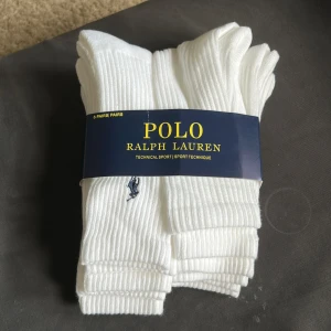 Vita ribbade strumpor Polo Ralph Lauren - Sexpack vita ribbade strumpor från Polo Ralph Lauren med klassisk broderad logga i mörkblått. Strumporna är höga och tillverkade i en mjuk bomullsblandning som andas. Perfekta för sport eller chill vardagsstil.