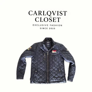 Quiltad jacka från Sebago  - Quiltad marinblå jacka från Sebago med broderad Tokyo-detalj på bröstet och röd logga på ryggen. Jackan har dragkedja framtill, ståkrage och två fickor med knappstängning. Perfekt för dig som gillar stilren och sportig look.