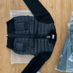 Svart quiltad jacka från Moncler - Snälla skriv innan ni köper!! Väldigt stilren och passar perfect till hösten. Snygg svart Moncler jacka med quiltad front och två stora fickor med knappar. Jackan har dragkedja och är tillverkad i en mix av stickat material och vadderad polyester. Perfekt för dig som vill ha en stilren och sportig look.
