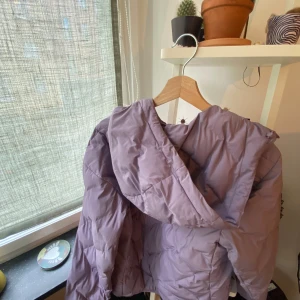 Ljuslila pufferjacka med huva - Säljer en ljuslila pufferjacka med huva och dragkedja. Jackan är quiltad och har en oversized vibe, perfekt för kalla dagar. Materialet är syntet och jackan har långa ärmar. Enkel och stilren design som passar till många outfits.