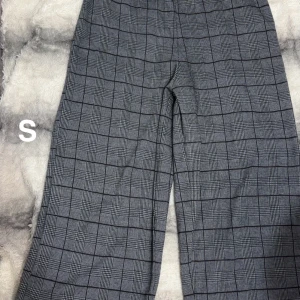 Grå rutiga kostymbyxor S - Snygga grå kostymbyxor med svart rutmönster. Byxorna har raka ben och klassisk passform, perfekta för en stilren look. Materialet känns mjukt och bekvämt, och de passar lika bra till sneakers som till boots. Sparsamt använda🌸 storlek s