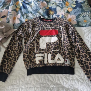 Leopardmönstrad Fila tröja - Säljer en leopardmönstrad tröja från Fila med stor logga framtill. Tröjan har svarta muddar vid ärmslut och nederkant, och är långärmad. Perfekt statement-plagg för dig som vill sticka ut med coolt mönster och sportig vibe.