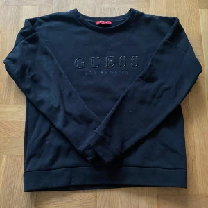 Svart sweatshirt från Guess - Svart sweatshirt från Guess med broderad logga på bröstet. Klassisk rund halsringning och långa ärmar. Perfekt basic med stilren look och diskret branding. Mjuk och bekväm, passar till allt.