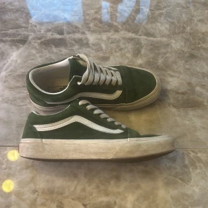 Gröna Vans Old Skool sneakers - Snygga gröna Vans Old Skool sneakers med klassisk vit sidorand och vit sula. Ovandelen är i mocka och de har vita snören. Perfekta för dig som gillar streetstyle och vill ha en skön och tidlös sko till vardags.