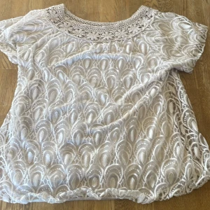 Beige spetsblus med kort ärm - Säljer en beige blus med vackert spetsmönster och rund halsringning. Blusen har korta ärmar och ett detaljerat virkat parti upptill. Perfekt för dig som gillar romantisk stil.