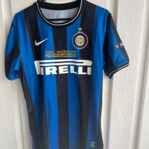 Inter Milan fotbollströja Sneijder 10 - Inter Milan matchtröja med blå och svarta ränder, Sneijder 10 på ryggen och Pirelli som sponsor på framsidan. Kortärmad modell med Nike-logga och Champions League-märke på ärmen. Perfekt för fans av klubben.