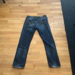 Blå jeans från Nudie Jeans - Säljer ett par klassiska blå jeans från Nudie Jeans med raka ben och orangea sömmar. Jeansen har fem fickor och en snygg läderpatch bak i midjan. Perfekta för dig som gillar en tidlös stil och vill ha ett par jeans som funkar till det mesta. Nypris på dessa runt 1199, mitt pris 299! Pris går att diskuteras! Hör av er vid minsta lilla fundering🤗