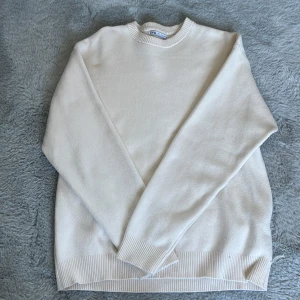Vit stickad tröja från Zara - Säljer en stilren vit stickad tröja från Zara med rund halsringning och ribbade muddar. Perfekt för en clean och enkel look. Passar dig som gillar klassiska plagg med en modern touch.