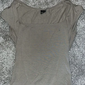 Beige topp med fyrkantig ringning från Gina Tricot - Säljer en beige topp från Gina Tricot i storlek XXS. Toppen har en snygg fyrkantig ringning och korta ärmar. Perfekt att matcha med jeans eller kjol för en enkel och stilren look.