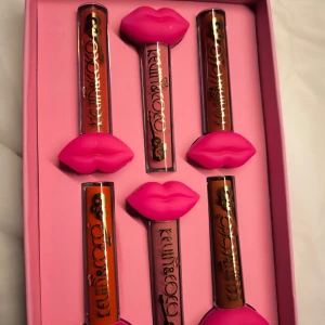 6 Pack mått Läppglans - Säljer ett set med sex matta läppglans från Kevin & Coco i olika nyanser av rött, rosa och nude. Förpackningen är rosa med coolt Rock & Roll-tryck och varje läppglans har ett lock format som rosa läppar. Perfekt för dig som vill ha flera färger att välja mellan.