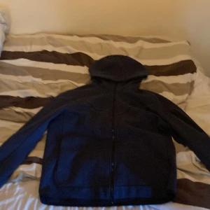 Blå hoodie från Nike - Säljer en mörkblå hoodie från Nike med dragkedja framtill och huva. Hoodien har lång ärm och är tillverkad i mjukt bomullsmaterial. Perfekt för dig som gillar sportig och avslappnad stil. Den har även ett litet hål i fickan som inte går igenom