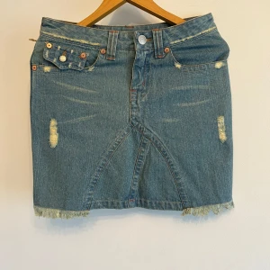 Jeanskjol från True Religion - Säljer ny jeanskjol från True Religion i klassisk blå denim. Kjolen har slitna detaljer, rå kant nertill och fickor både fram och bak. 💕