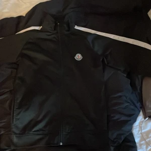 Svart jacka från Moncler - Säljer en svart jacka från Moncler med dragkedja och diskret logga på bröstet. Jackan har en sportig look med lång ärm och stilrena detaljer. Perfekt för dig som gillar klassisk och clean stil.