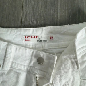 Vita jeansbyxor från ICHI - Säljer ett par vita jeansbyxor från ICHI med klassisk femficksdesign och raka ben. Byxorna har dragkedja och knapp framtill samt diskreta sömmar på bakfickorna. Perfekta för en fräsch och stilren look.