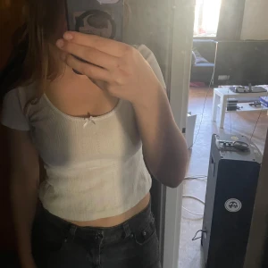 Vit croppad ribbad topp med rosett - Säljer en söt vit croppad topp med ribbad struktur och liten rosettdetalj framtill. Toppen har korta ärmar och rund halsringning. Perfekt till sommaren! Toppen är från bikbok och storlek S🥰💕