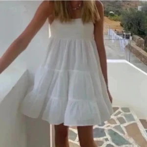 Vit somrig klänning med volang - Säljer en söt vit klänning med volang och luftig passform. Klänningen har smala axelband och är kort i modellen, perfekt för varma dagar. Enkel och stilren design som passar till många tillfällen.