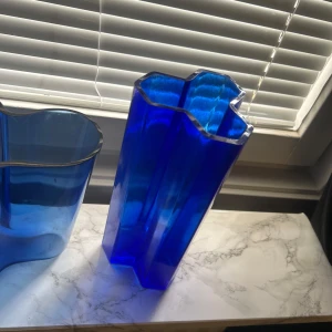 Mörkblå Alvar Aalto. vas - Säljer en ikonisk blå Alvar Aalto vas från Iittala. Vasen har en organisk, vågformad design och är tillverkad i blått glas. Perfekt som inredningsdetalj eller för blommor. Klassisk skandinavisk design