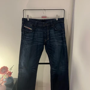 Mörkblå Diesel Larkee jeans - Säljer ett par mörkblå Diesel Larkee jeans med klassisk femficksdesign och snygga slitningar. Jeansen har raka ben och kontrastsömmar, samt en liten logga på fickan fram. Perfekta för dig som gillar en tidlös jeansstil.