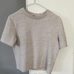 Beige stickad topp med pärlor från Zara - Superfin beige stickad topp från Zara med korta ärmar och pärldetaljer framtill. Perfekt för dig som vill ha något enkelt men ändå med en twist. Rund halsringning och mjukt material.