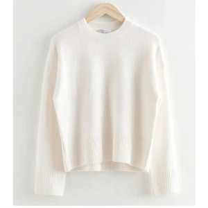 Vit stickad tröja med rund hals - Säljer en enkel och stilren vit stickad tröja med rund hals och långa ärmar. Tröjan har ribbade muddar vid ärmslut och nederkant, perfekt för lager-på-lager under kyliga dagar.