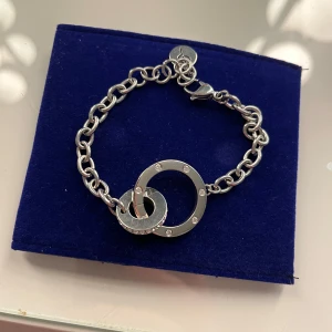 Armband från Edblad - Säljer ett stilrent armband i silverfärg med två sammanlänkade cirklar och grov kedja. Perfekt accessoar för att lyfta din outfit med en modern touch.