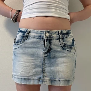 Ljusblå jeanskjol med slitningar - Säljer en ljusblå jeanskjol med snygga slitningar och tvättad effekt. Kjolen har klassiska fem fickor, knapp och dragkedja framtill samt dekorativa sömmar på bakfickorna. Perfekt för en avslappnad och trendig look.