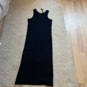 Svart ribbad långklänning från 157 - Säljer en svart ribbad långklänning från 157 i 100% bomull. Klänningen är ärmlös med rund halsringning och har en tight passform. Perfekt för dig som gillar en stilren och enkel look.