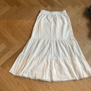 Vit långkjol med broderade blommor - Säljer en  vit långkjol med broderade blommor och volang. Kjolen har resår i midjan och är tillverkad i ett lätt bomullstyg. Perfekt för dig som gillar en feminin och luftig stil. Jag skulle säga att dom e ganska små i storlekarna så jag skulle kunna tänka min att det skulle passa i s-xs