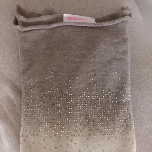 Beigemelerad tröja med strass från Minority - Supersnygg beigemelerad tröja från Minority med lång ärm och glittrande strassdetaljer framtill. Tröjan har en mjuk ombre-effekt från mörkare beige till ljust och är tillverkad i en skön blandning av viskos, polyester och elastan. Liten i storlek mer XS-S