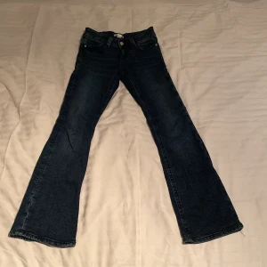 Mörkblå bootcut jeans från Gina Tricot - Säljer ett par mörkblå bootcut jeans från Gina Tricot. Jeansen har klassisk femficksdesign, silverfärgade knappar och dragkedja. Snyggt utsvängda ben och normal passform, perfekta till vardagsstilen.