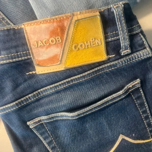 Jacob Cohen jeans - Jacob Cohen jeans gjorda i italien, de har blivit använda men är i bra skick. Den enda defekten är att patchen är lite sliten men annars är de i toppskick. De har en sliten look och en fin blå färg. Skriv till mig vid funderingar