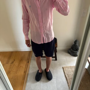 Rosa skjorta från Ralph Lauren (pris diskuteras)  - Säljer en ljusrosa skjorta från Ralph Lauren med klassisk krage och knäppning framtill. Skjortan har lång ärm och är tillverkad i ett tunt, luftigt linnematerial. Den har en broderad blå logga på bröstet och en avslappnad passform.