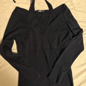 Svart ribbad klänning Bik Bok - Svart långärmad klänning från Bik Bok med ribbad nederdel och djup v-ringning. Klänningen har halterneck-detalj och är figurnära med stretchigt material. Perfekt för dig som gillar stilren och enkel look.