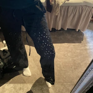 Svarta byxor med hålmönster och snörning - Säljer ett par svarta byxor med hålmönster över hela benen och snörning i midjan. De har en avslappnad passform och är perfekta för dig som vill sticka ut lite extra. Superbekväma och lätta att styla till olika outfits. Från nelly