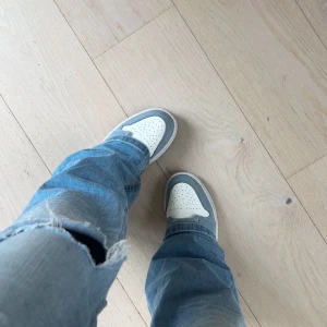 Nike Air Jordan 1 Mid blå/vit - Nike Air Jordan 1 Mid i en clean färgkombo av vitt, ljusblått och marinblått. Klassisk high-top siluett med perforerad tå, snörning och ikoniska Air Jordan-detaljer på sidan. Ovandel i skinn och syntet.   Skorna är köpta för lite mindre än ett år sen , men sparsamt använda och i bra skick. Undersidan har ingen slitning. (Skorna tvättas noggrannare vid köp)